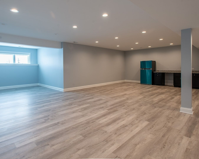 Empty finished basement with wood flooring, a small window, and built-in cabinets and refrigerator.
