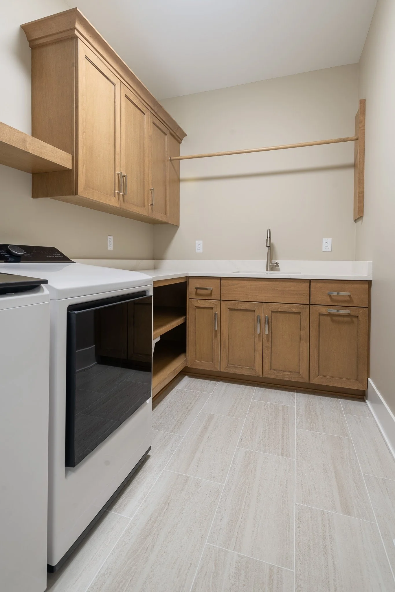 Kitchen with light wood cabinets, a white countertop, a stainless steel sink, and a white stove. There are three electrical outlets on the wall and the floor is tiled with beige rectangular tiles.