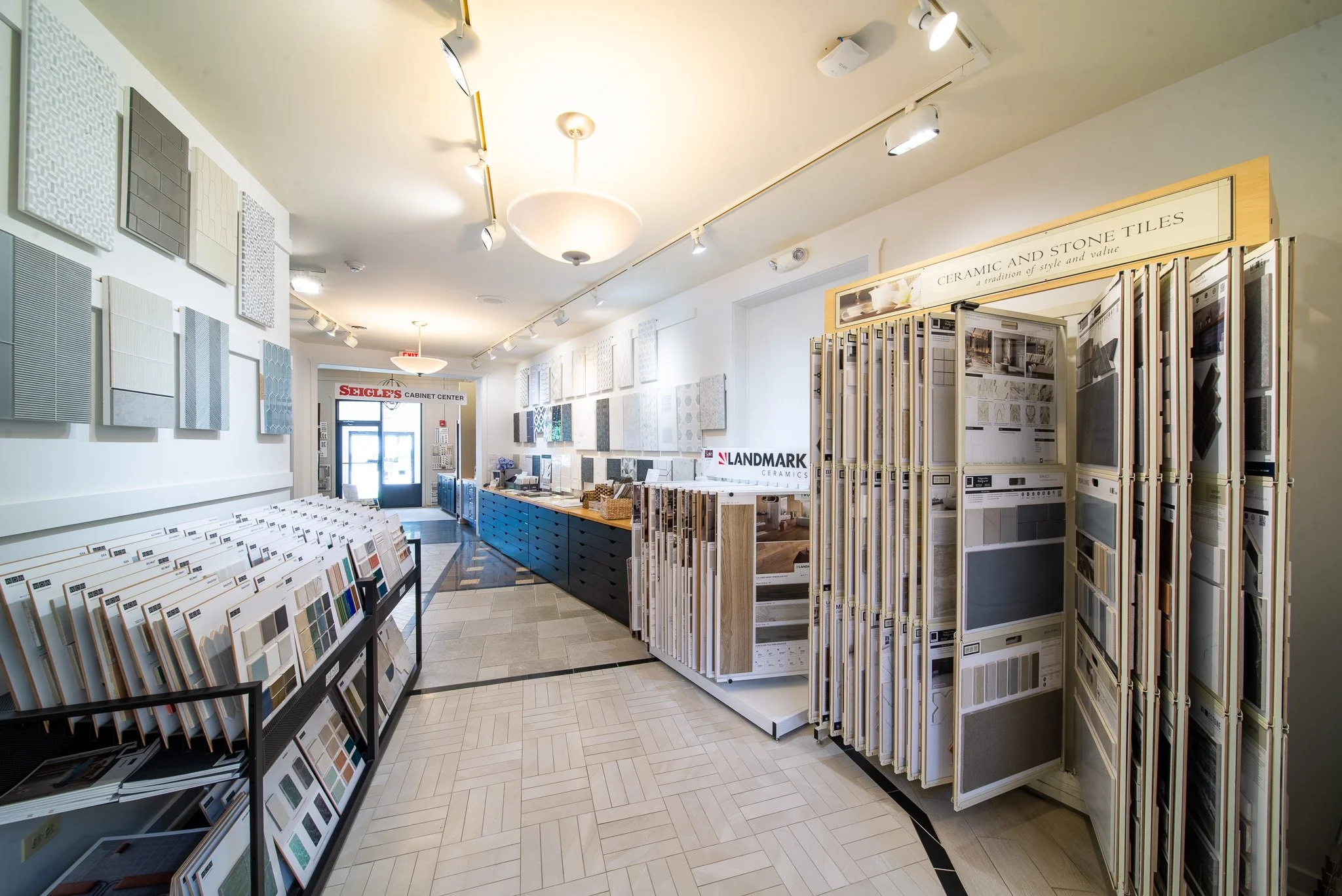 Interior of a tile and stone store with displays of tile samples on shelves and walls, and flooring samples on display racks.
