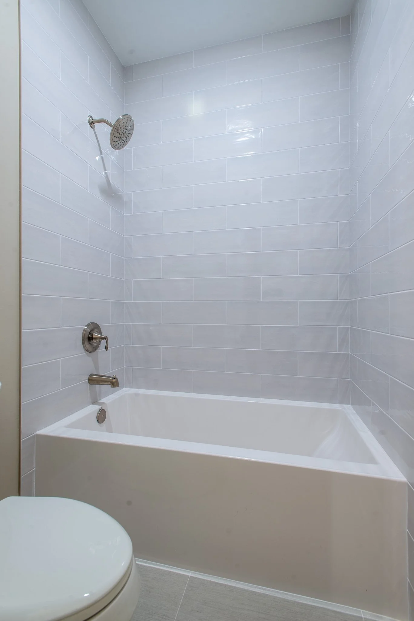 Bathroom with white tiled walls, bathtub, showerhead, and toilet.