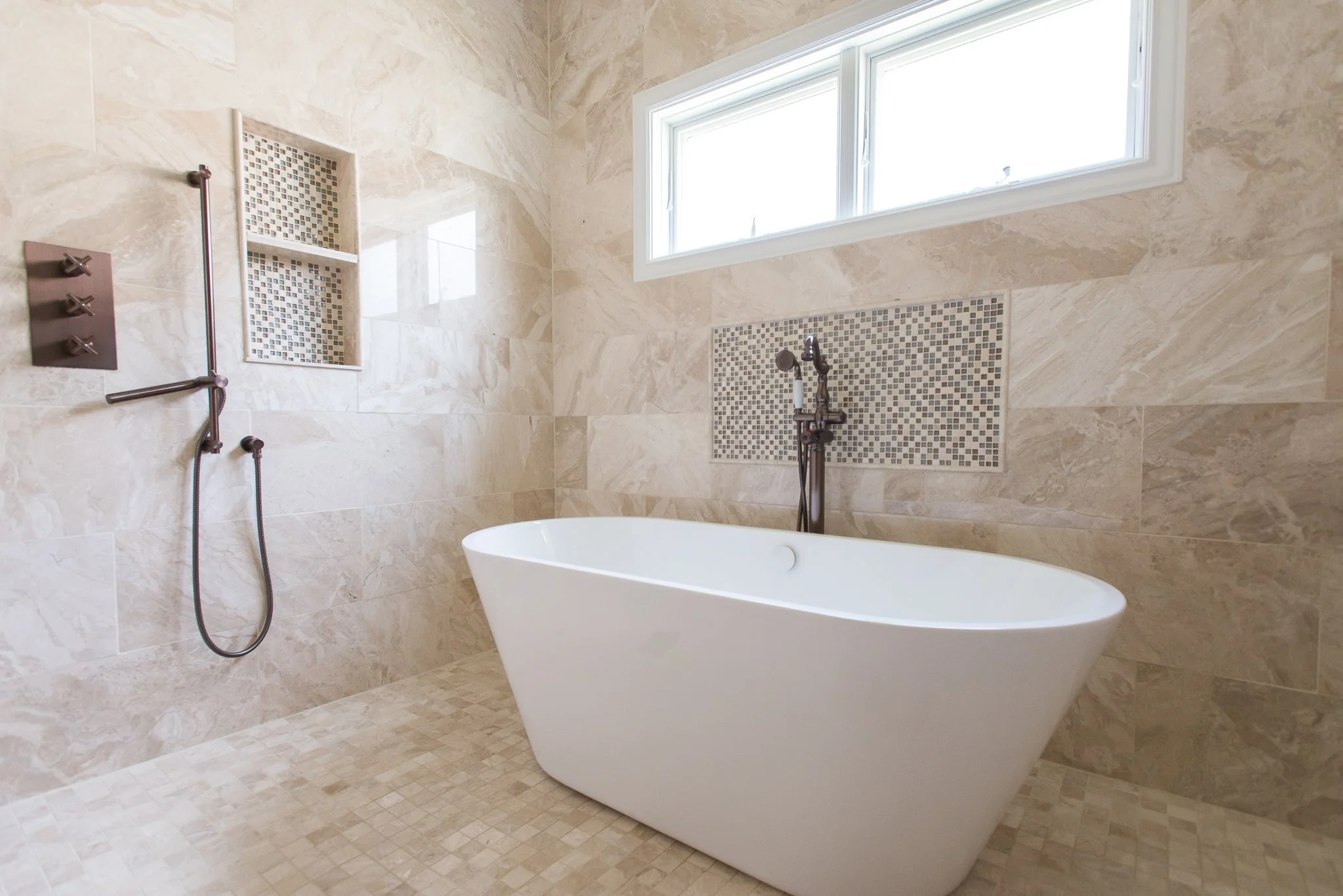 Modern bathroom with beige marble tiles, a freestanding bathtub, and a window allowing natural light.