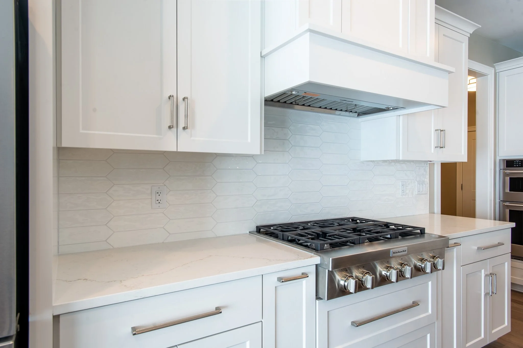 Modern white kitchen with cabinets, a marble countertop, a stainless steel gas stove, and a white hexagonal tile backsplash.