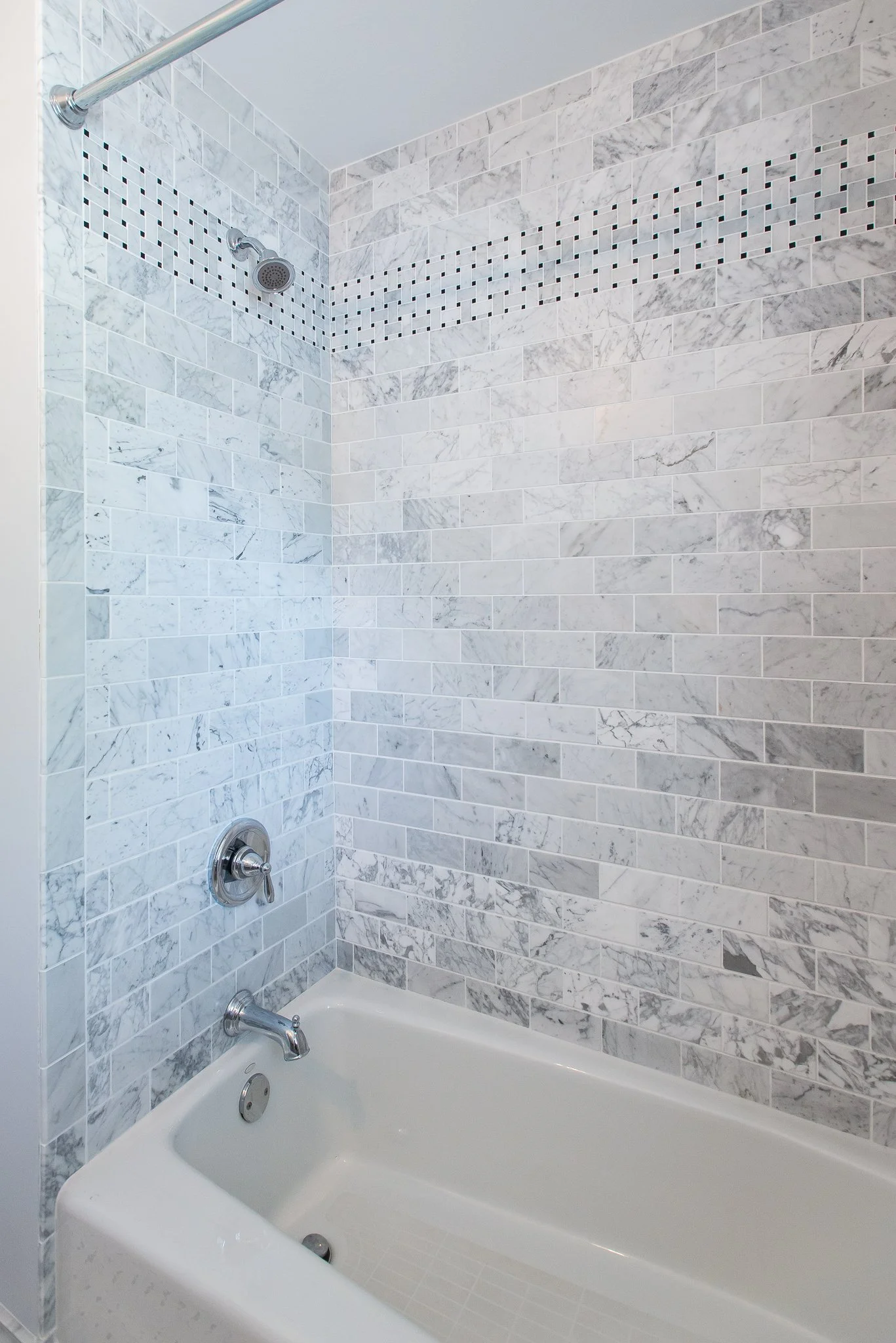 A bathroom shower area with white and gray marble tile walls and a built-in bathtub.