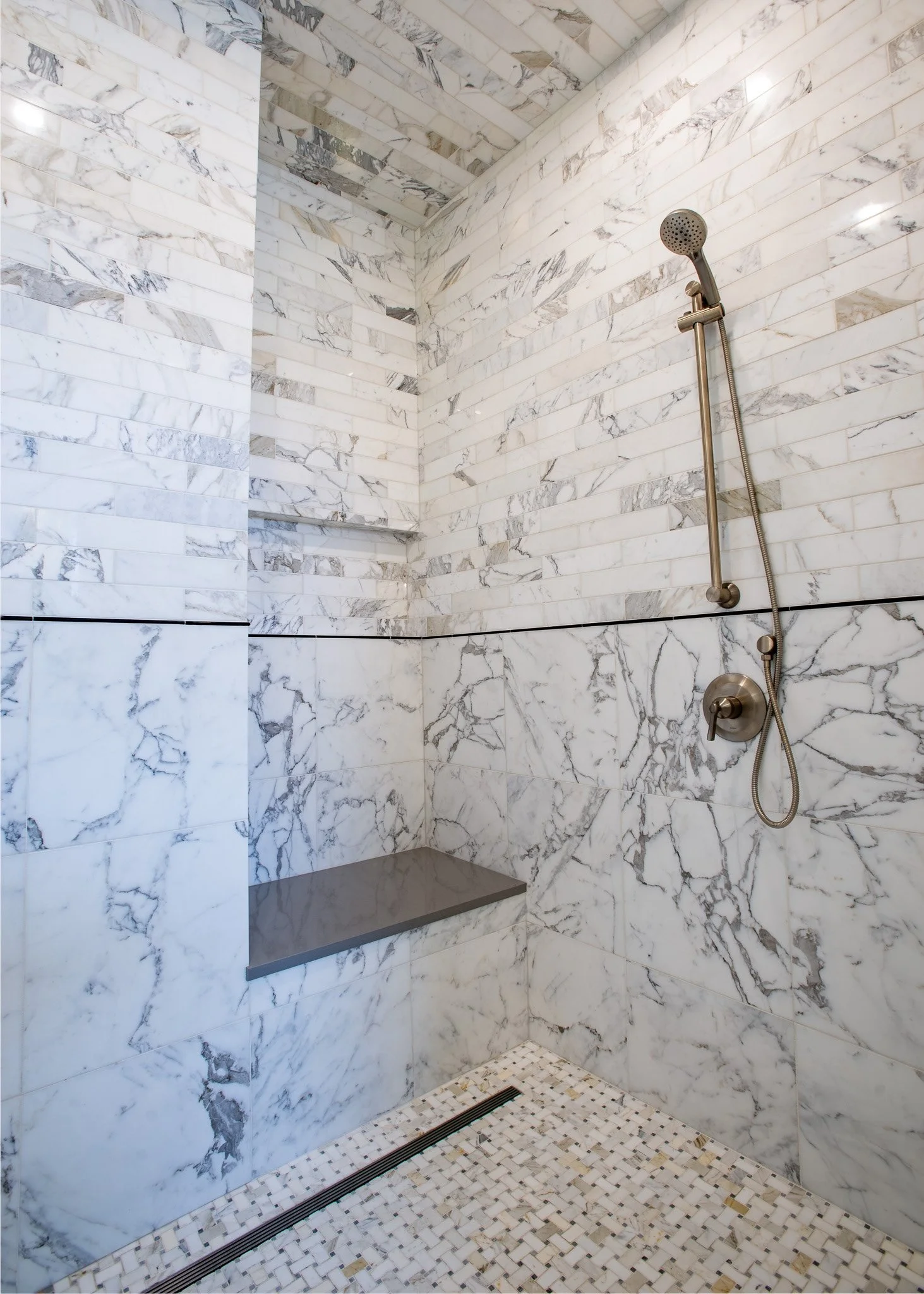 A marble shower with a handheld showerhead, a built-in bench, and a tiled floor with a linear drain.