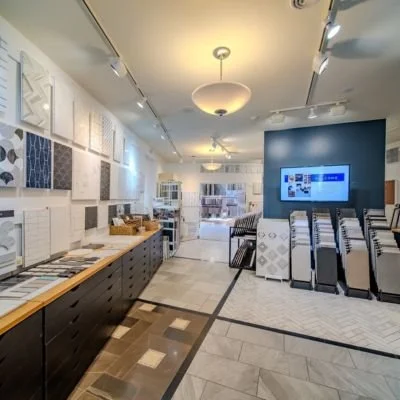Showroom with sample tiles and flooring options displayed on walls and tables, with a seating area and a large screen on the blue wall.