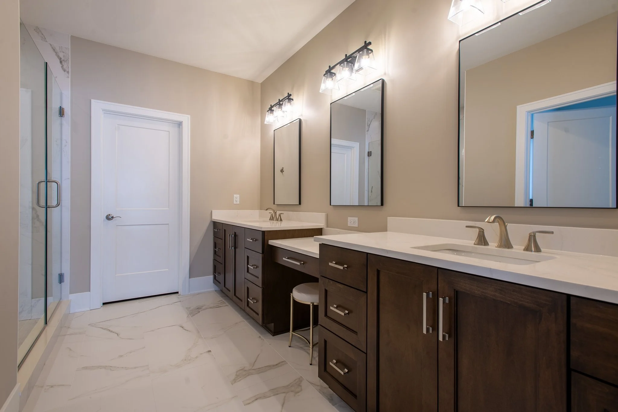 Modern bathroom with double vanity, large mirrors, wall-mounted light fixtures, and a walk-in shower with glass door.