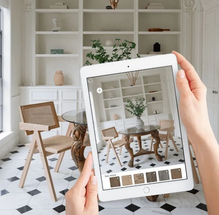 Person taking a photo of a dining room with tablet, showing a round glass table, four wooden chairs, and a white built-in bookshelf.