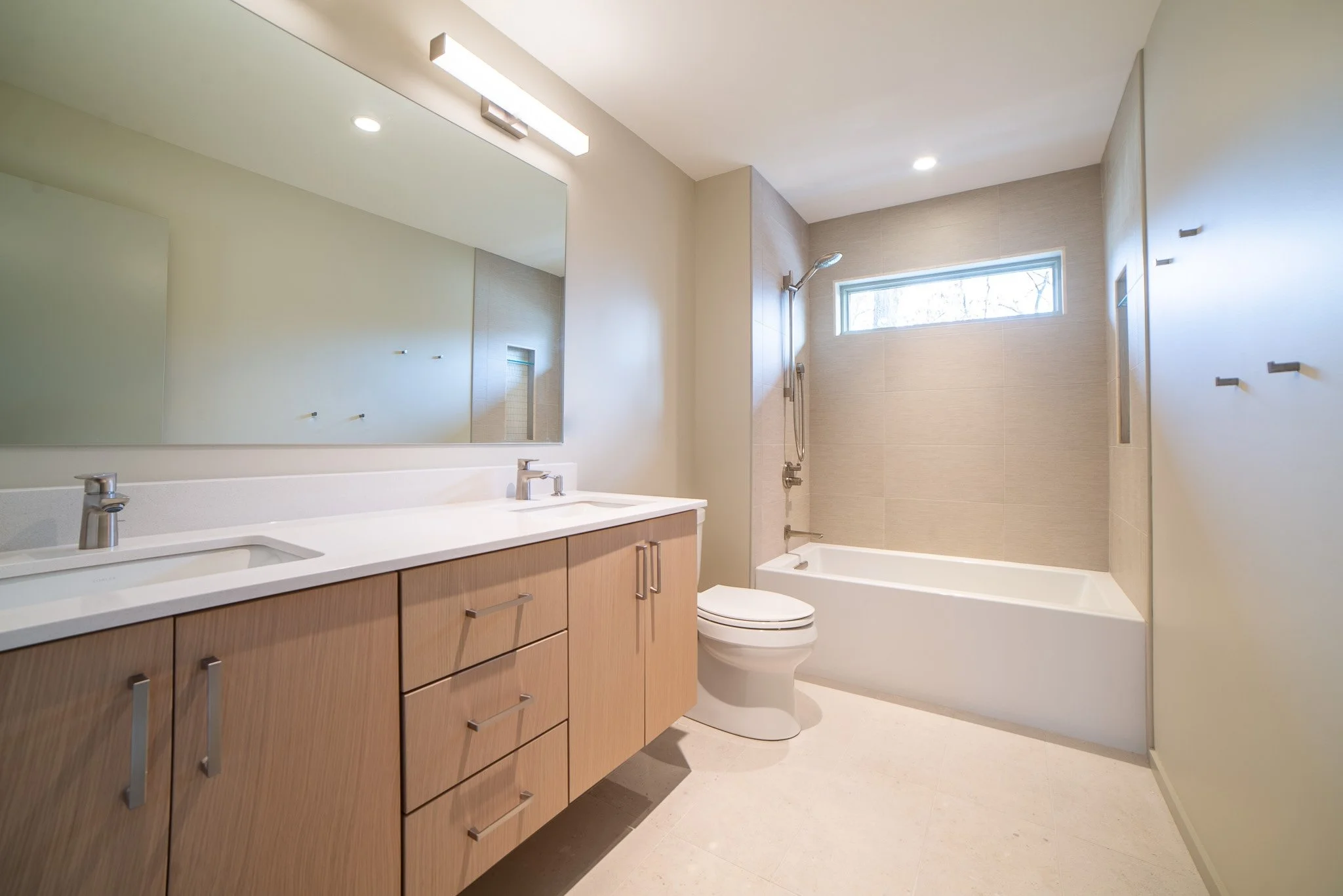 Modern bathroom with a double sink vanity, large mirror, near a bathtub with a window, neutral color scheme.