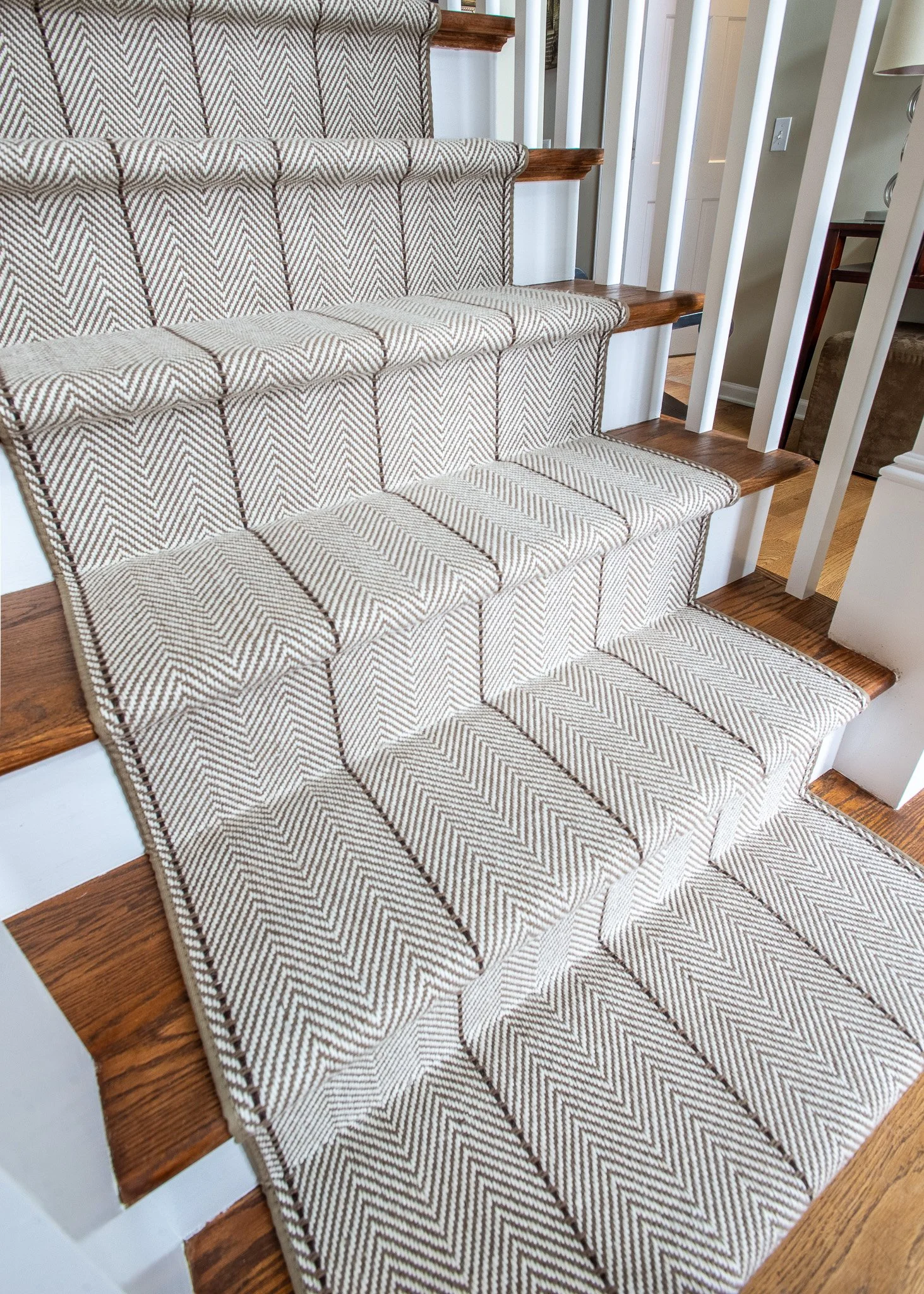 Carpeted staircase with beige and brown zigzag pattern, wooden steps, white railing, and hardwood flooring.