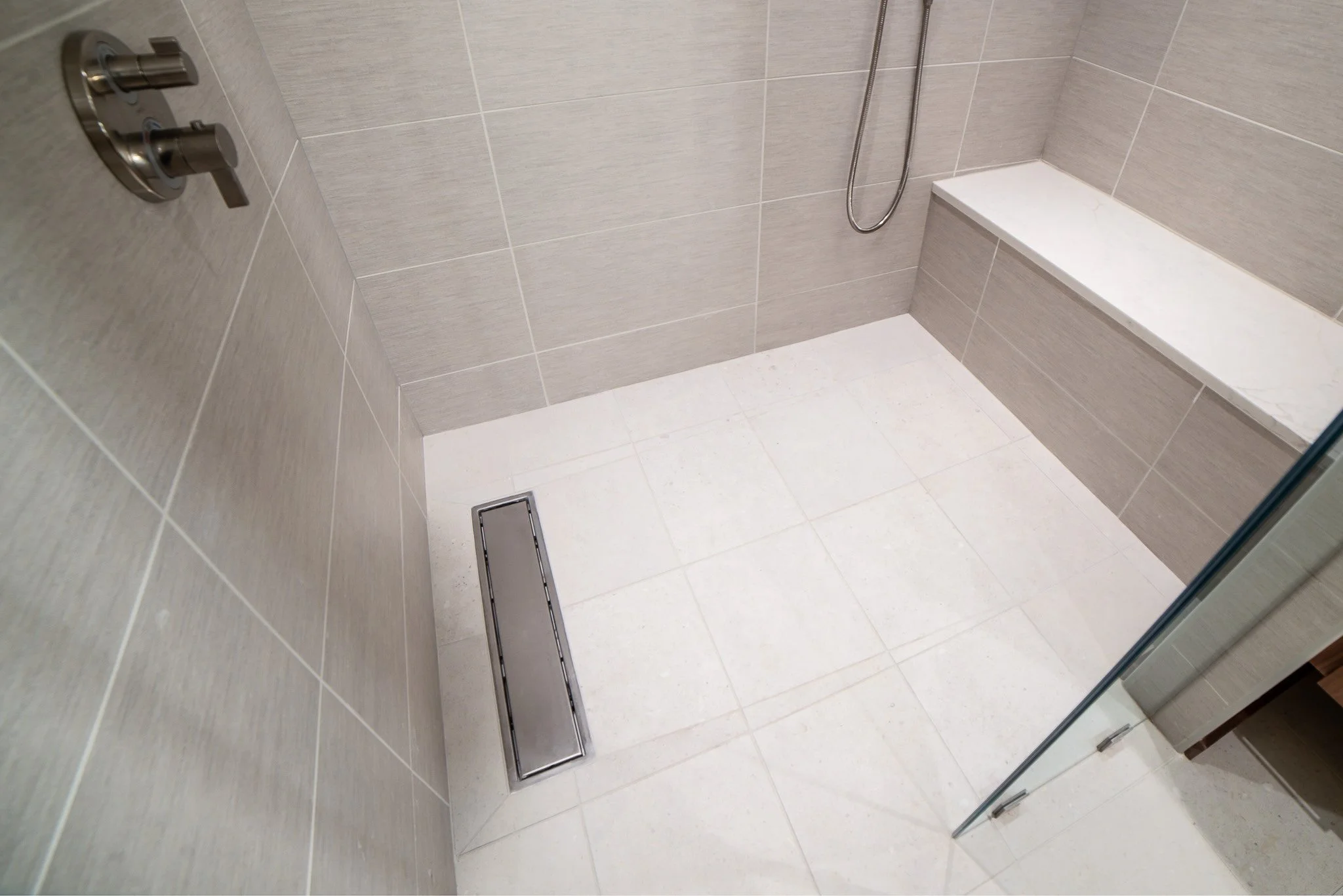 A tiled shower area with a built-in bench, a handheld showerhead, and a linear drain on the floor.
