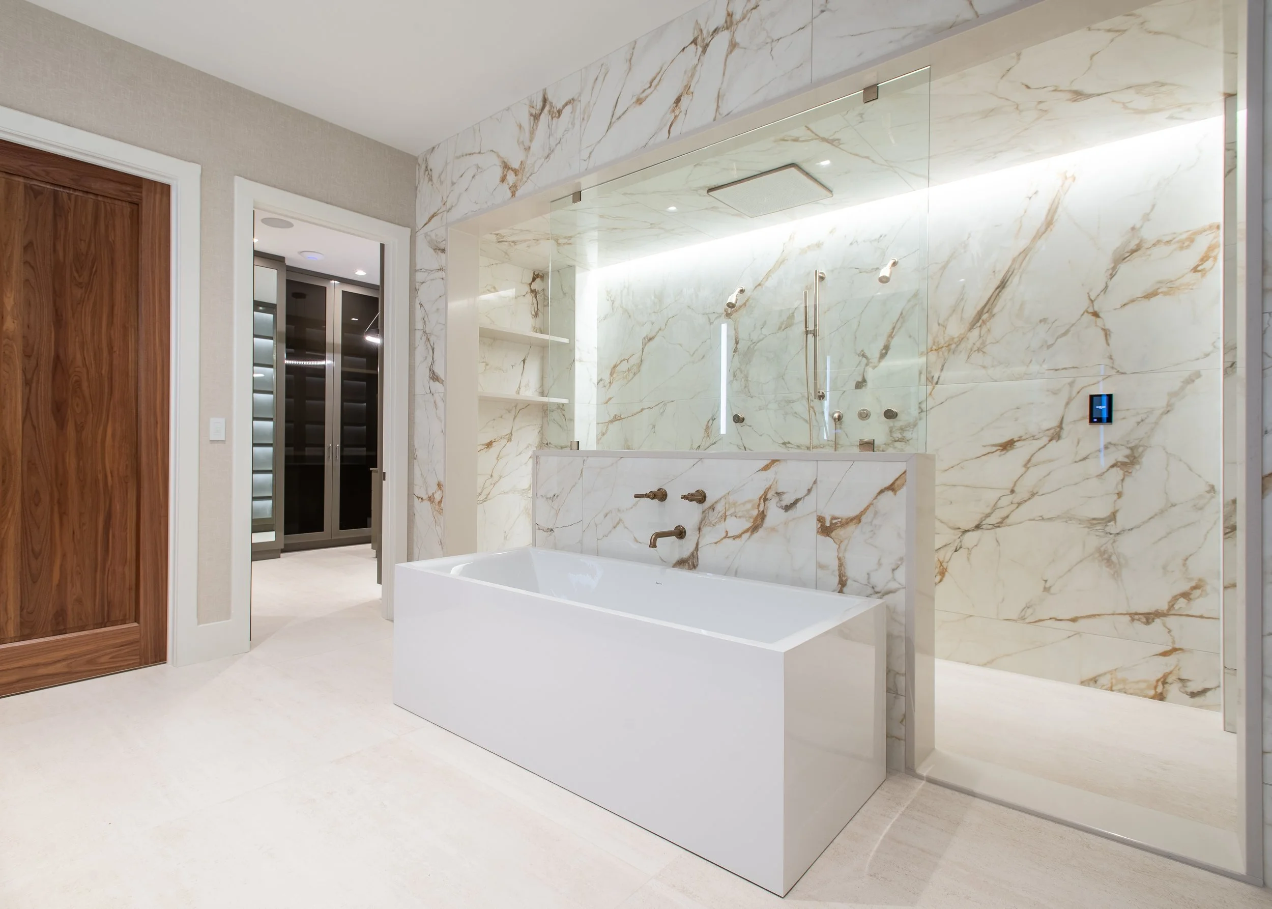 Modern bathroom with marble walls and floor, a white bathtub, and a walk-in shower with glass enclosure and marble walls.