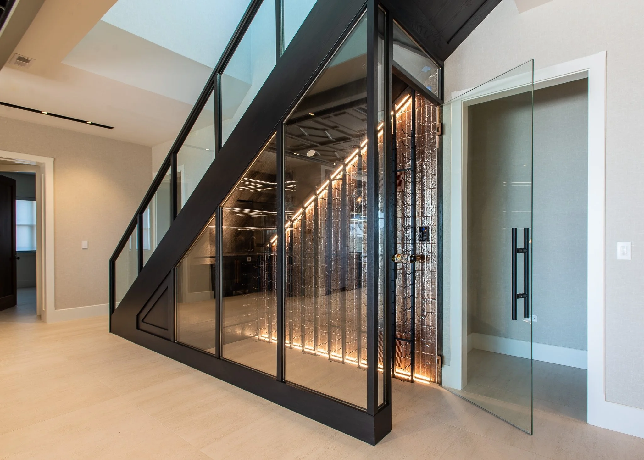 Modern glass enclosure with black framing and interior lighting, adjacent to a glass door, in a contemporary home interior.
