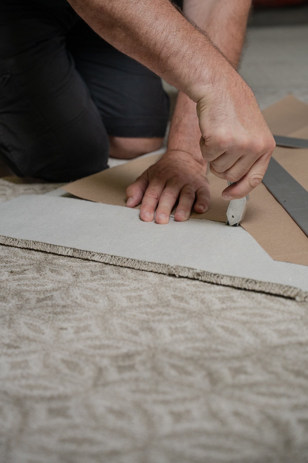 Person cutting a carpet with a utility knife on the floor.