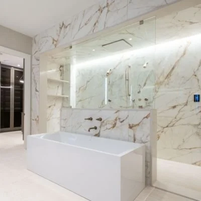 Modern bathroom with a white bathtub, marble walls, and a large mirror.