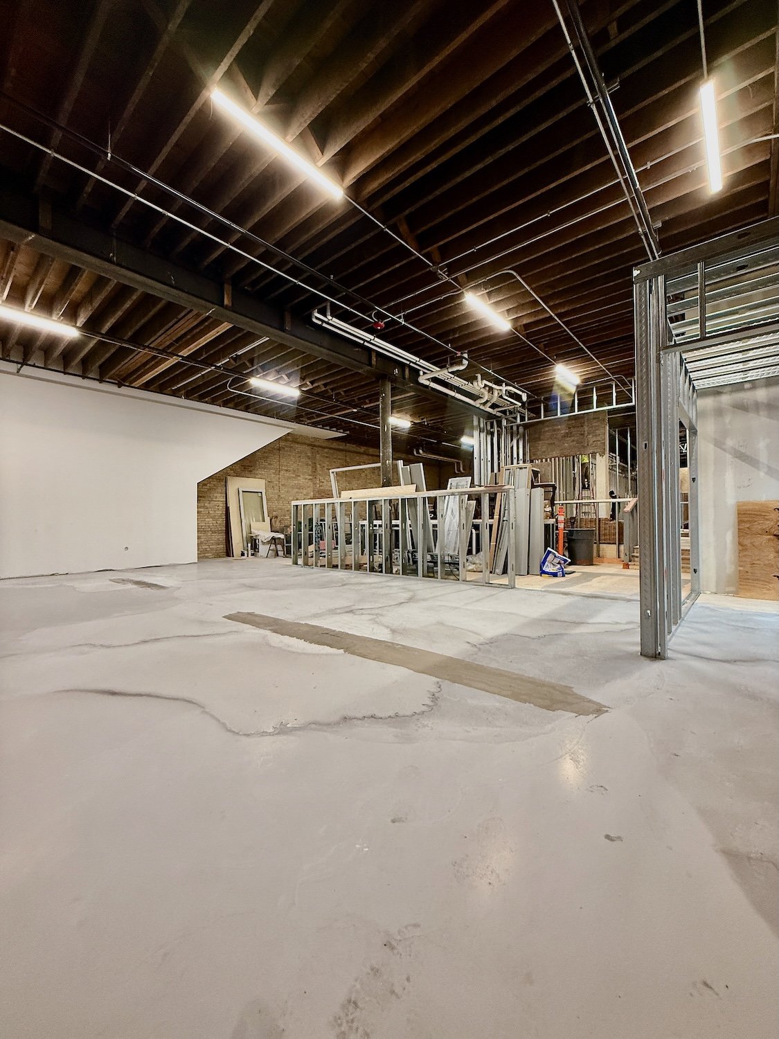 Interior of a building under construction with exposed wooden ceiling, metal framing, and unfinished concrete floor.