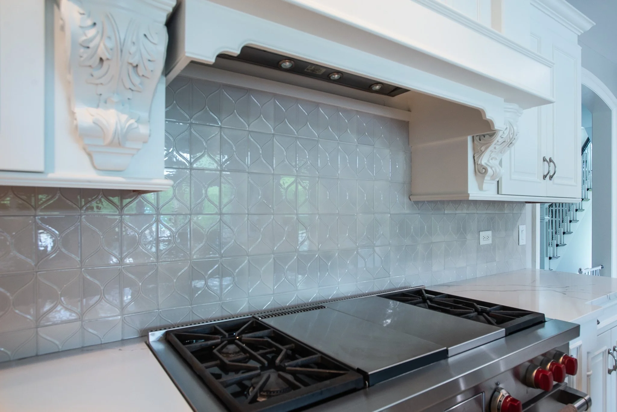 White kitchen with decorative molding, a backsplash with patterned tiles, a stove with red control knobs, and a power outlet on the wall.