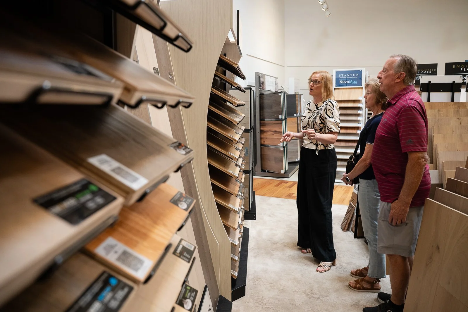 Three people browsing flooring samples in a showroom, with one woman explaining options to an older couple.