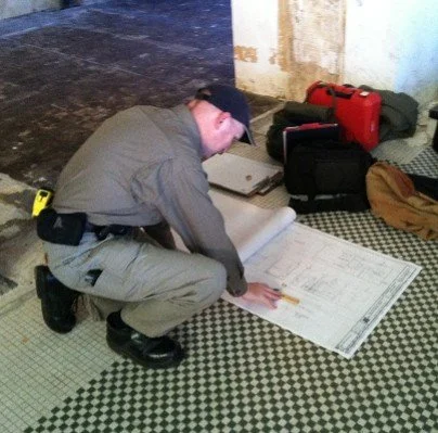 Person in uniform examining architectural plans on the floor.