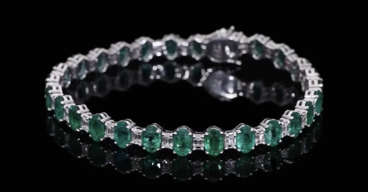 A silver bracelet with green gemstones and clear diamonds on a black reflective surface.