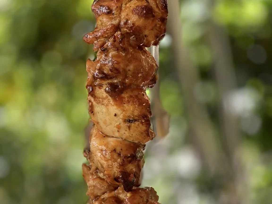 Kozis Chicken Kokobongo. Close-up photo of a grilled skewer with chunks of meat, likely chicken, against a blurred green background.