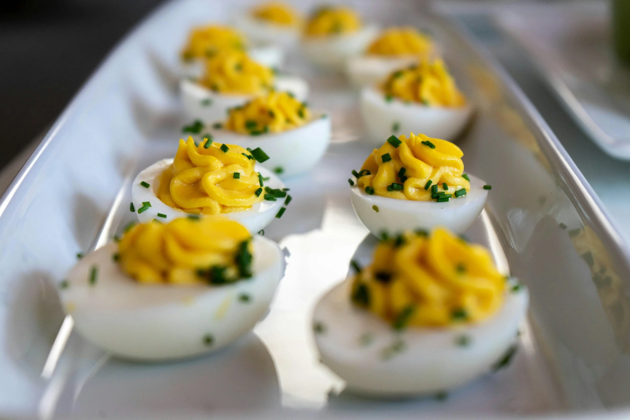 Close-up of deviled eggs topped with yellow yolk mixture and chopped green herbs, arranged in a row on a serving tray.