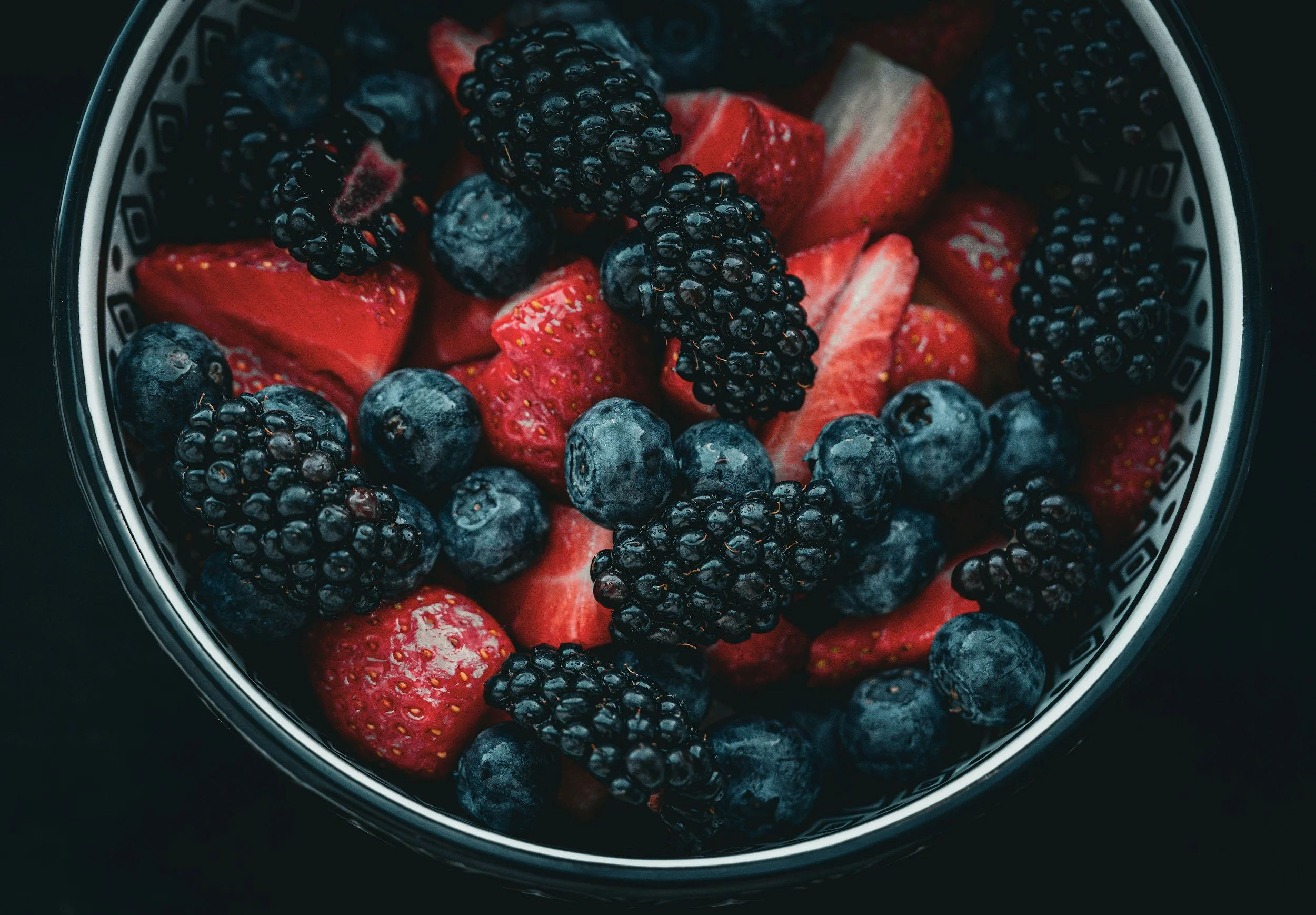 Close-up of a bowl filled with sliced strawberries, blueberries, and blackberries.