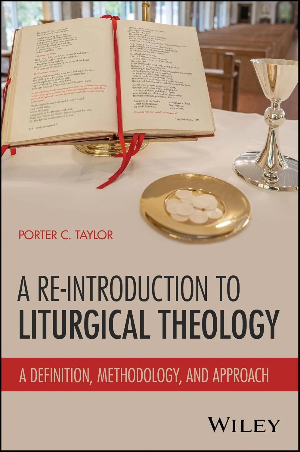 Book titled "A Re-Introduction to Liturgical Theology" by Porter C. Taylor on a table with a gold cross on its cover, an open Bible, a gold chalice, and a gold plate with communion wafers in a church setting.