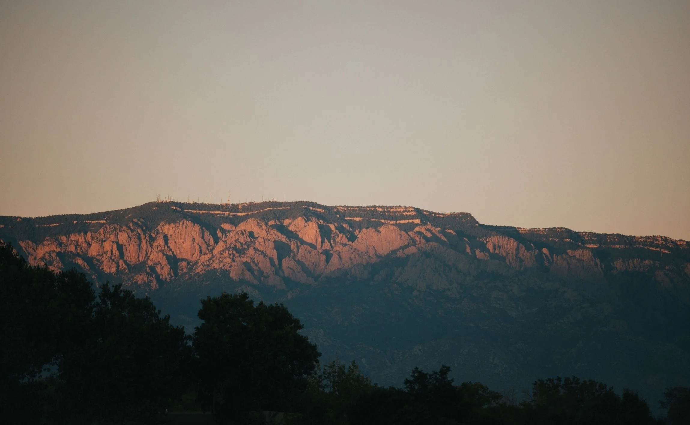 Sunset over rugged mountains with some trees in foreground.