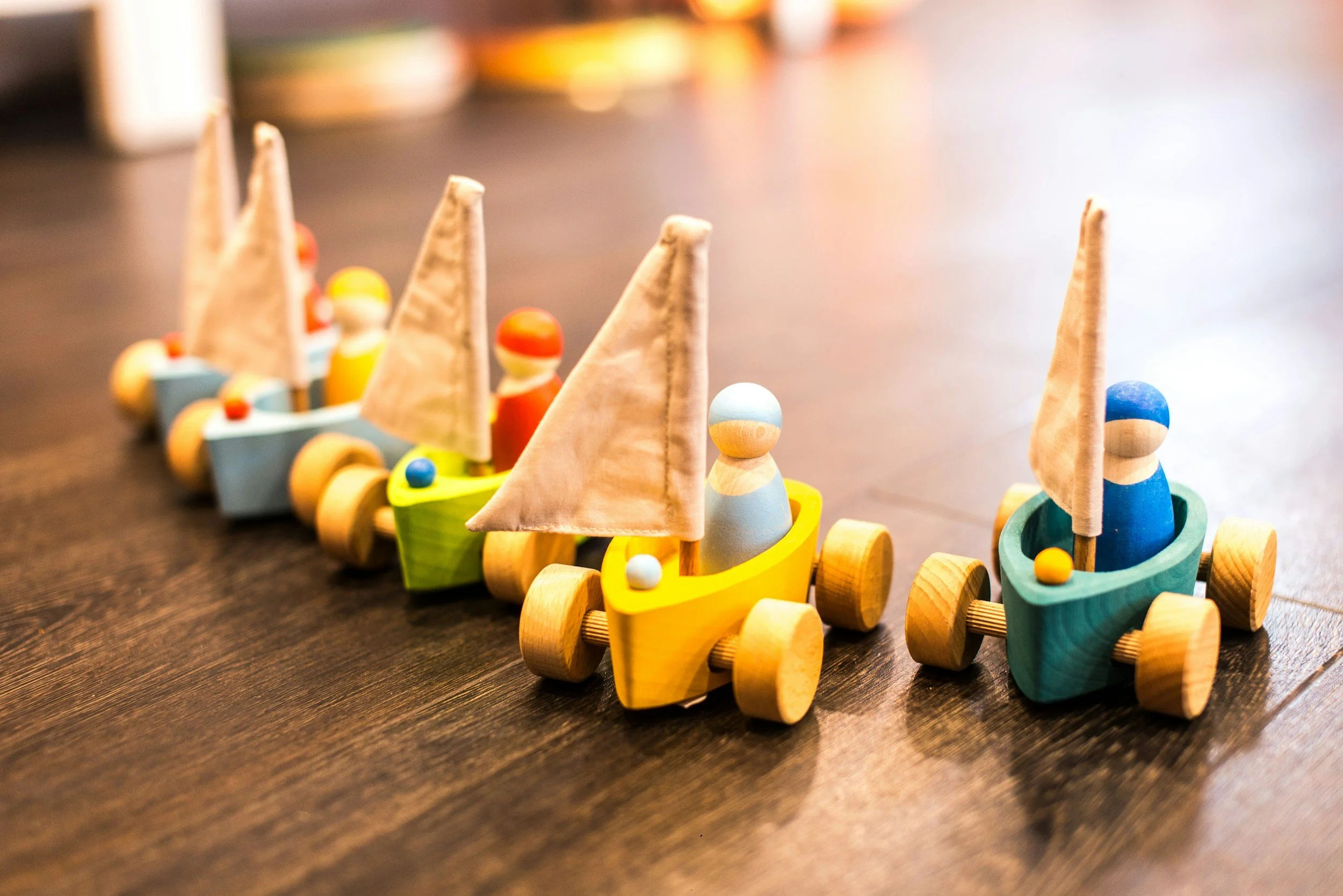 Colorful wooden toy boats with small sailboats on a dark wooden surface.