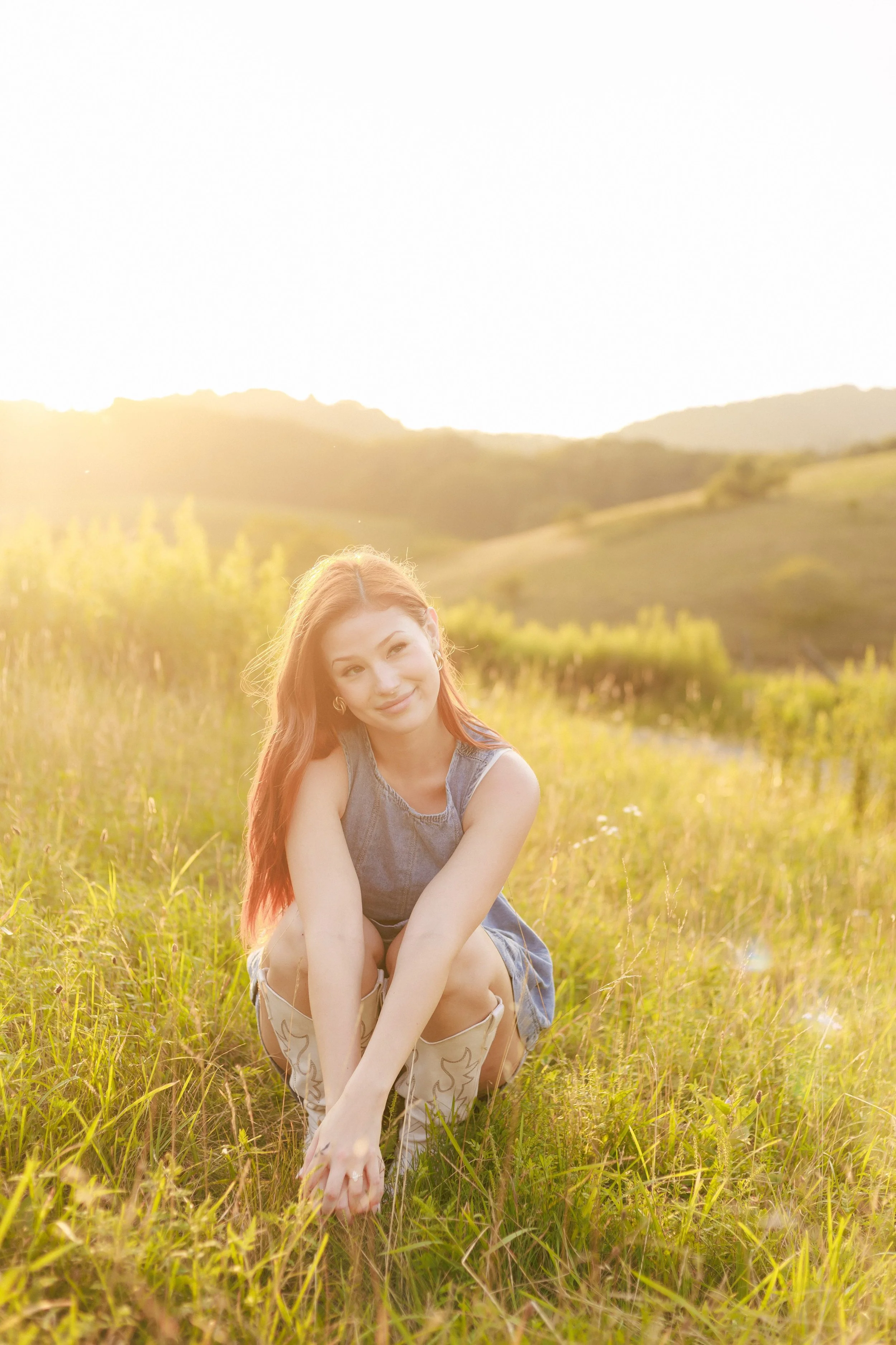 girl squatting down in a field with sun behidn her