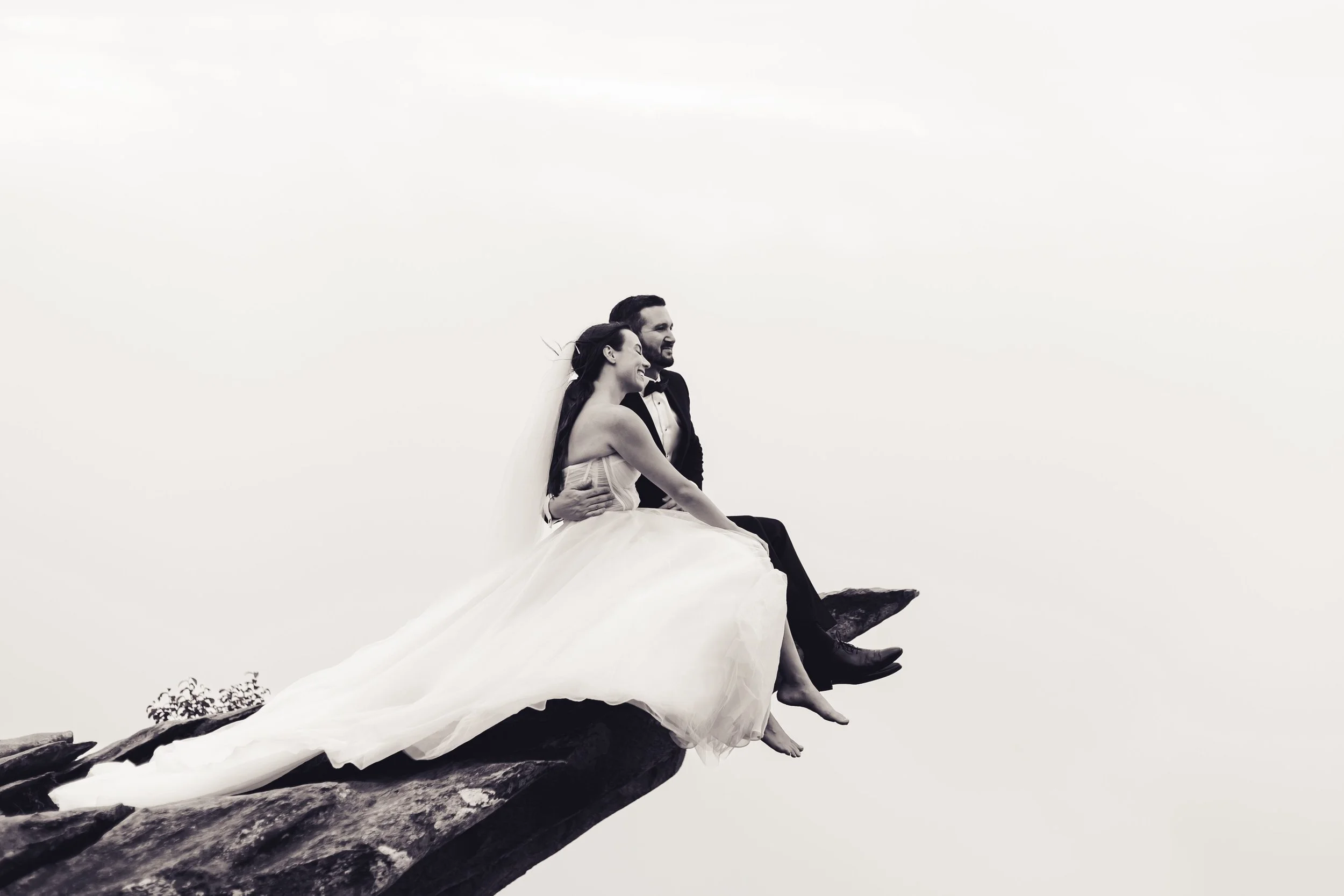 Bride and Groom sitting on a rock with their feet hanging off