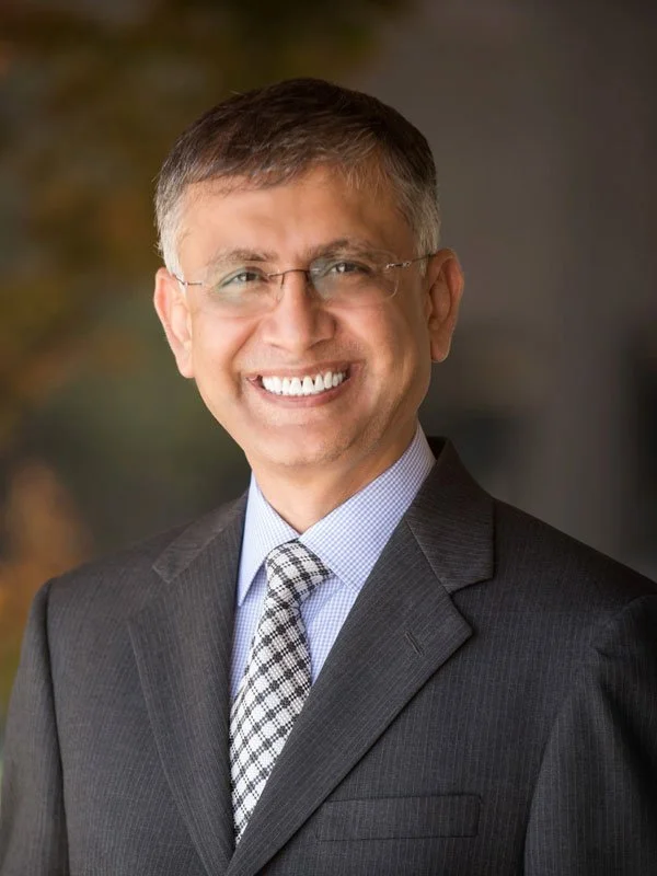 A smiling man in a suit and tie with glasses.