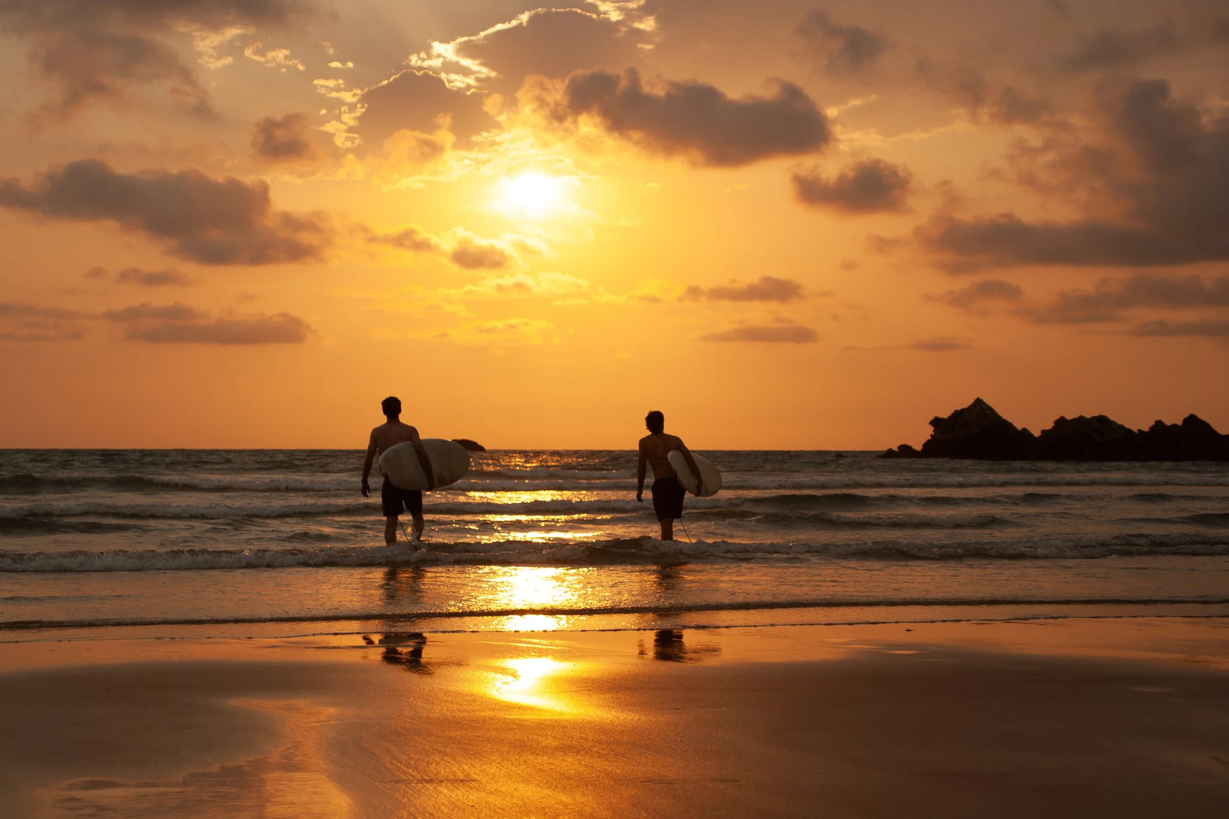 Editorial travel photograph of two surfers entering the ocean at sunset in Biarritz, capturing the relaxed freedom of Atlantic summer life.