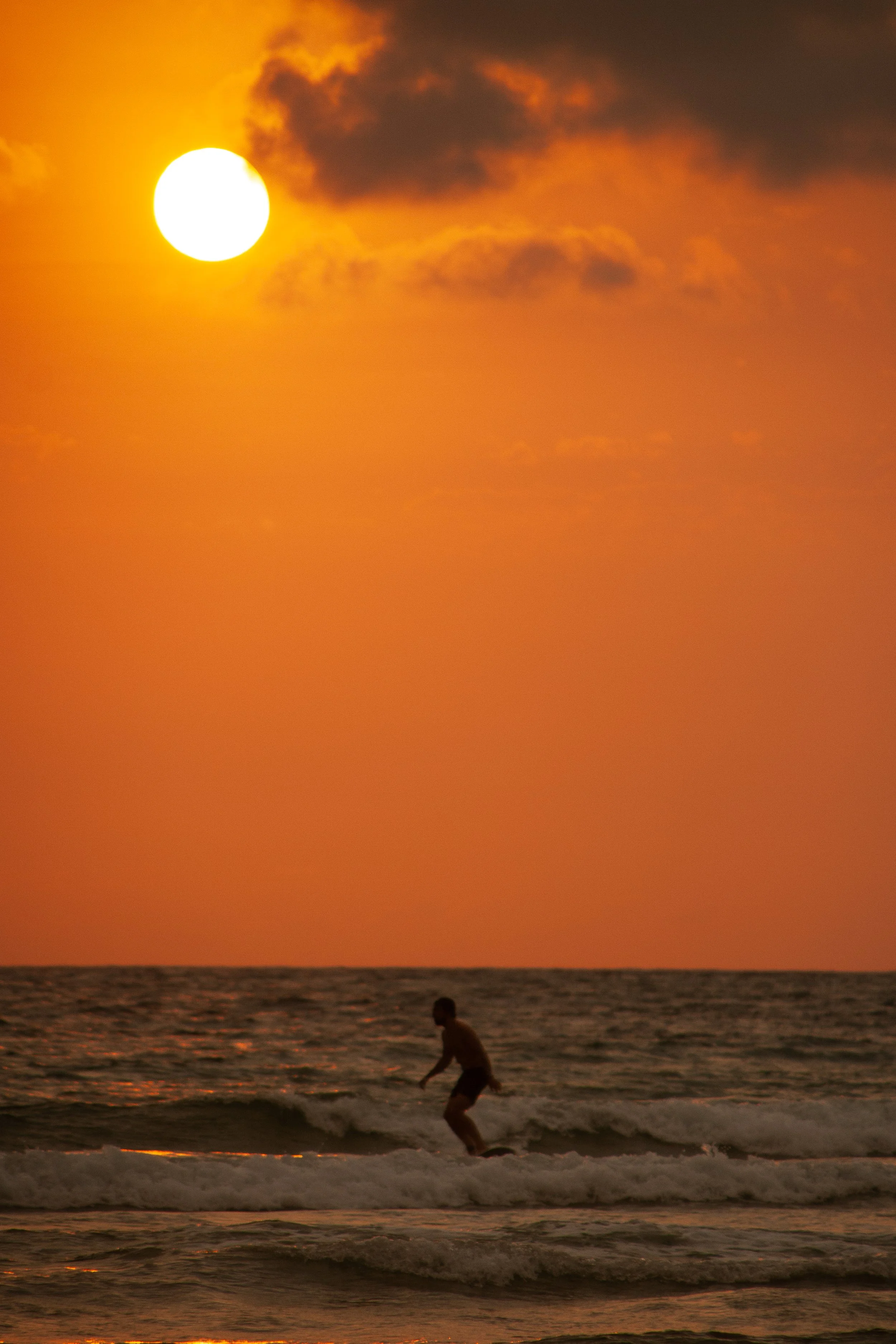 Luxury surf lifestyle photography in Biarritz, with a lone surfer riding a wave beneath an intense Atlantic sunset.