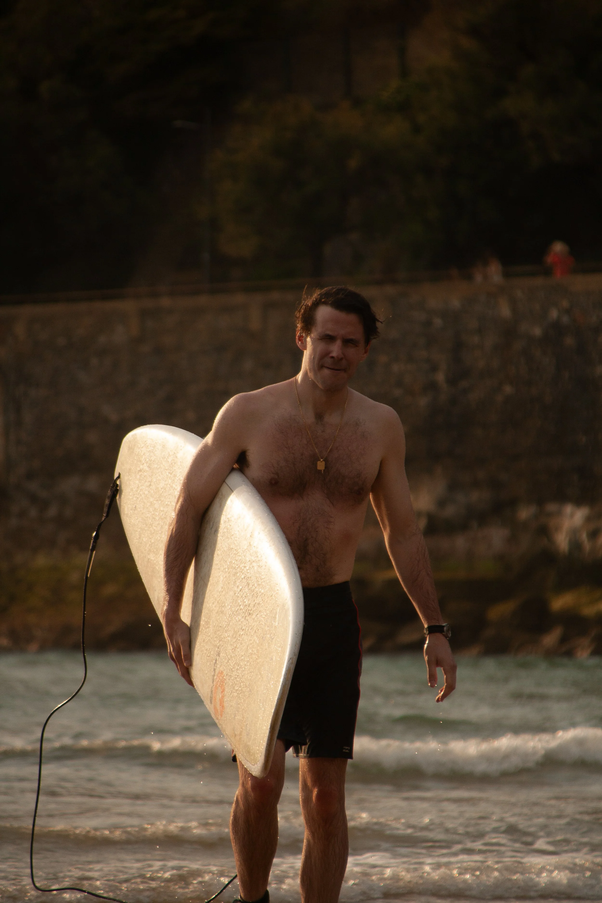 Editorial surf portrait in Biarritz, capturing a male model leaving the ocean with his surfboard in warm golden-hour light.