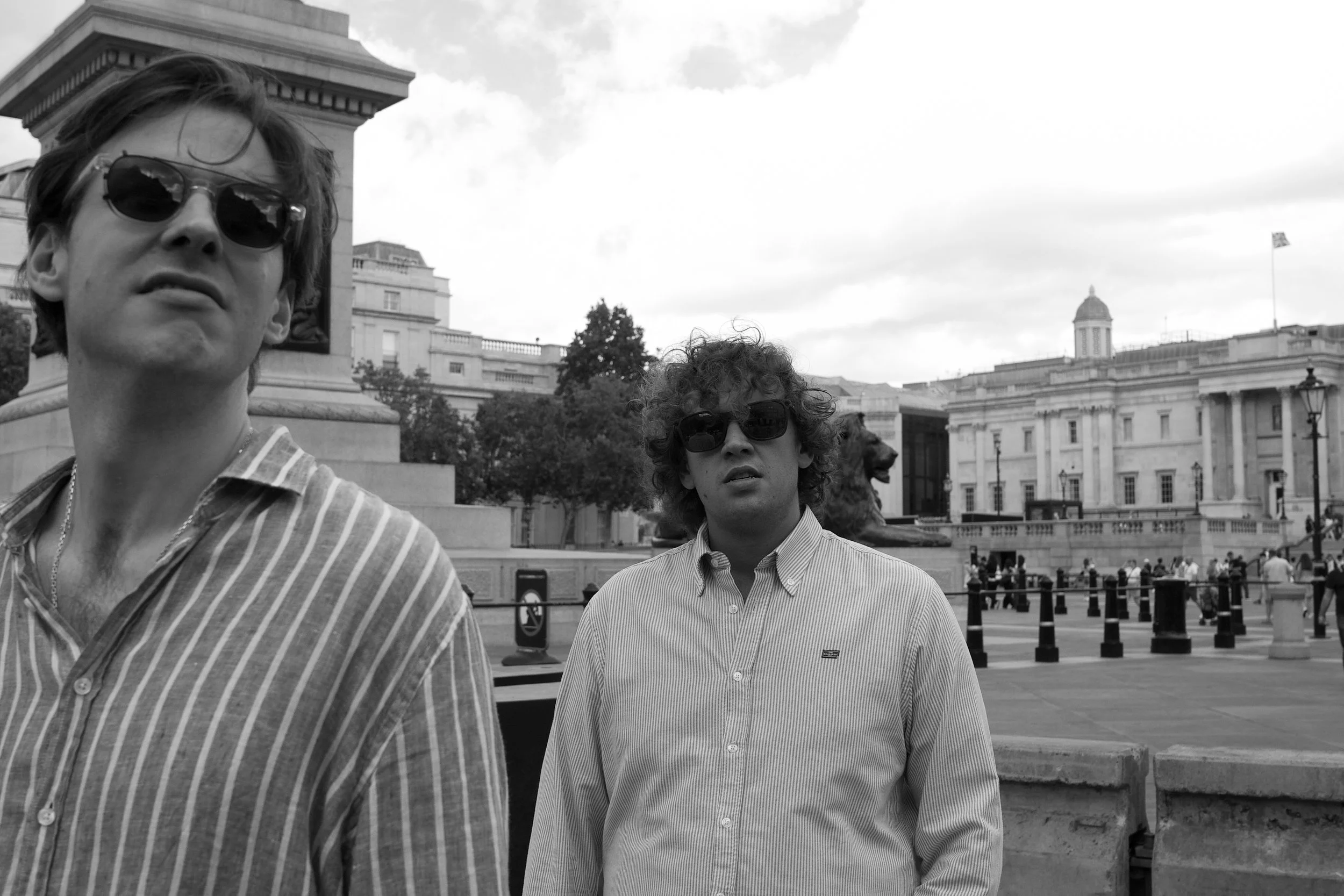 Editorial portrait of two music artists in Trafalgar Square, London, combining relaxed styling, sunglasses and an effortless contemporary attitude.