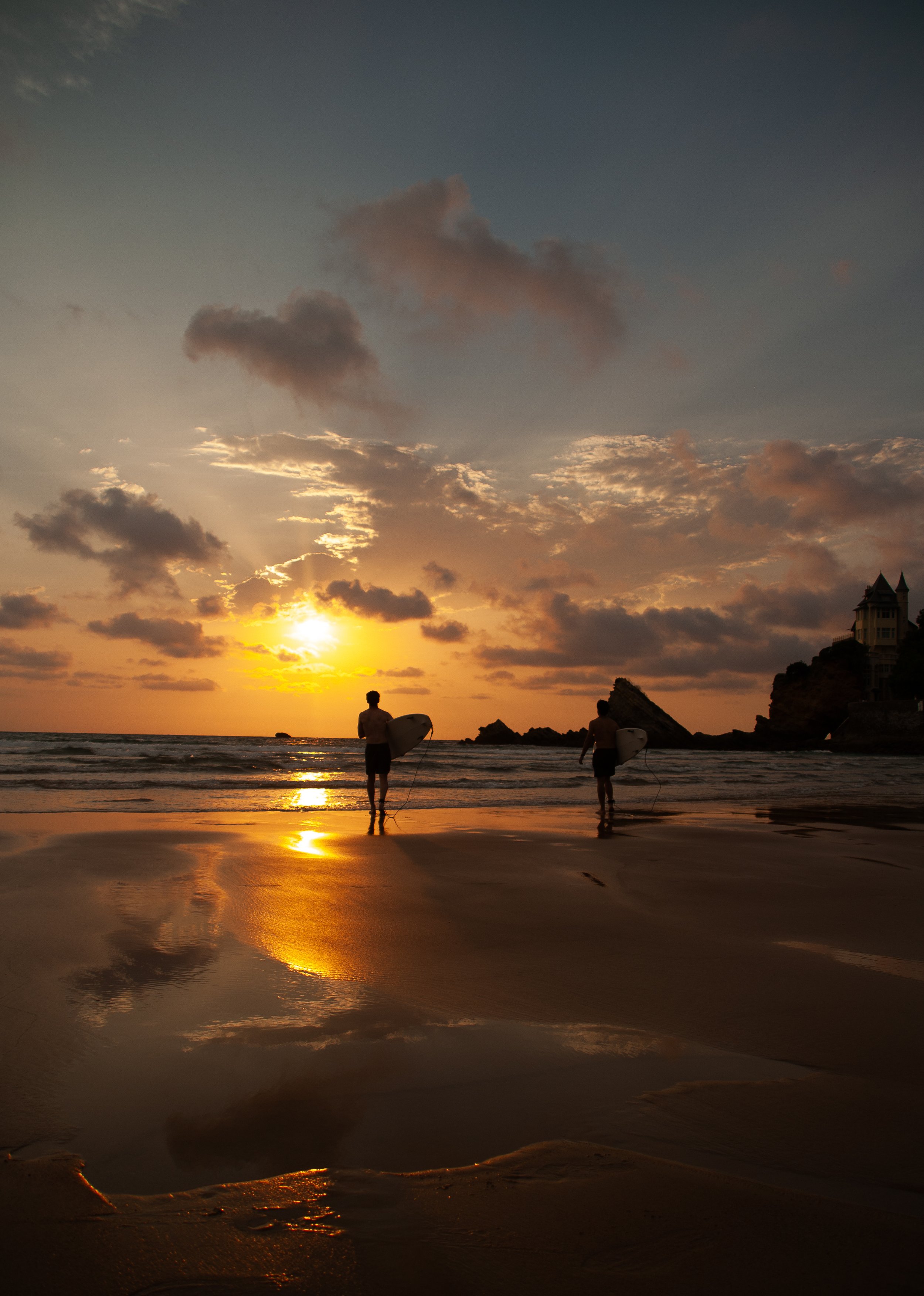 Candid surf lifestyle photography in Biarritz, with two surfers walking toward the Atlantic beneath a golden sunset.