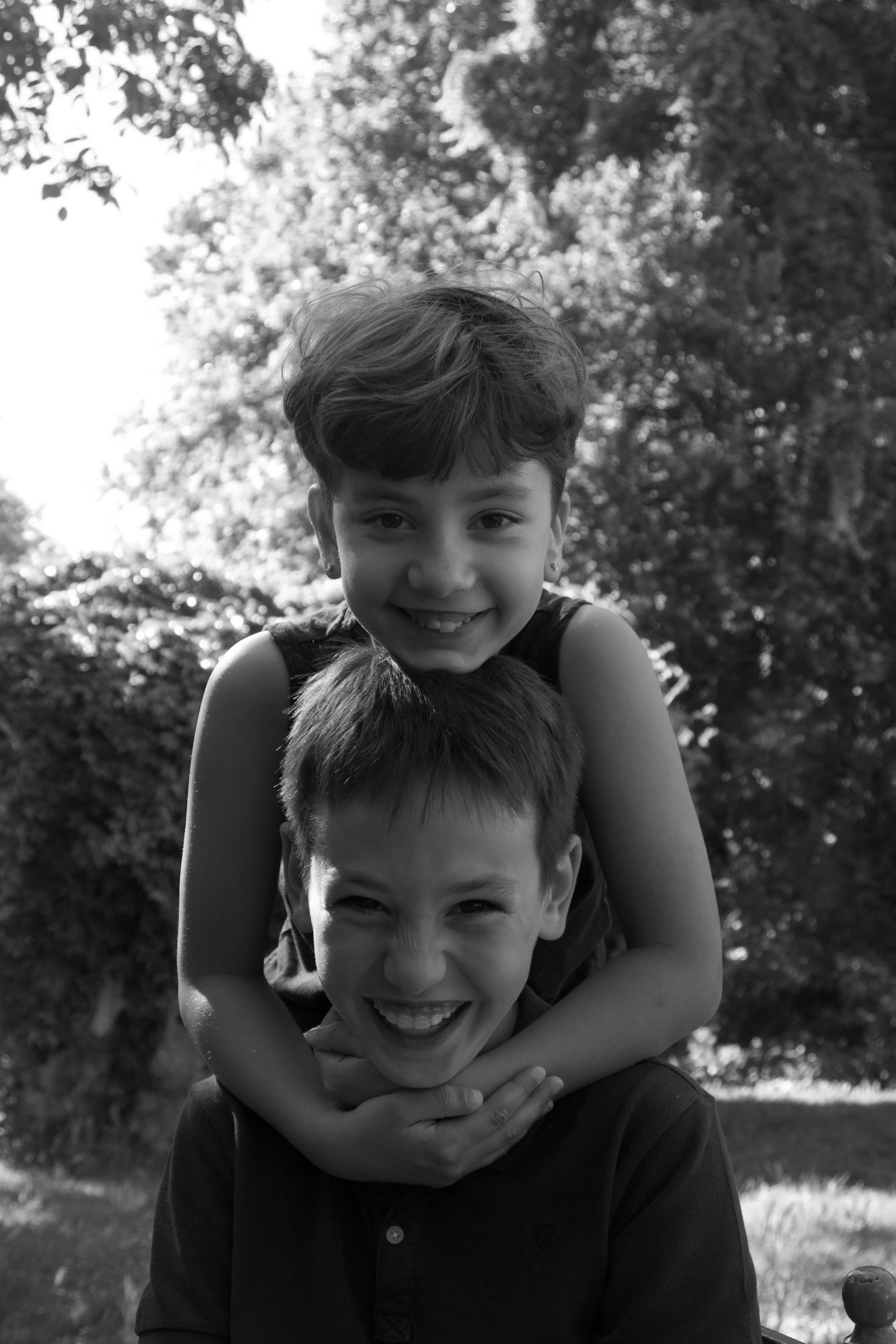 Playful children’s portrait of two siblings laughing together outdoors, photographed naturally during a relaxed family session.