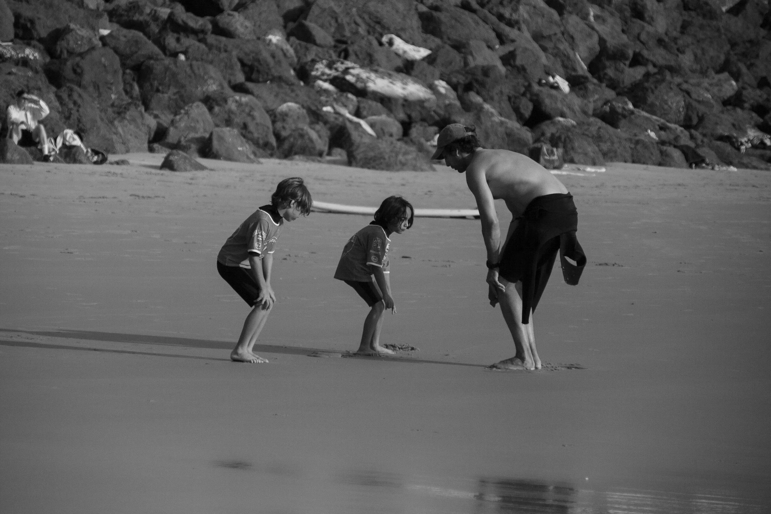 Candid family beach photograph in Biarritz, capturing a playful moment between an adult surf professor and two children on the sand.