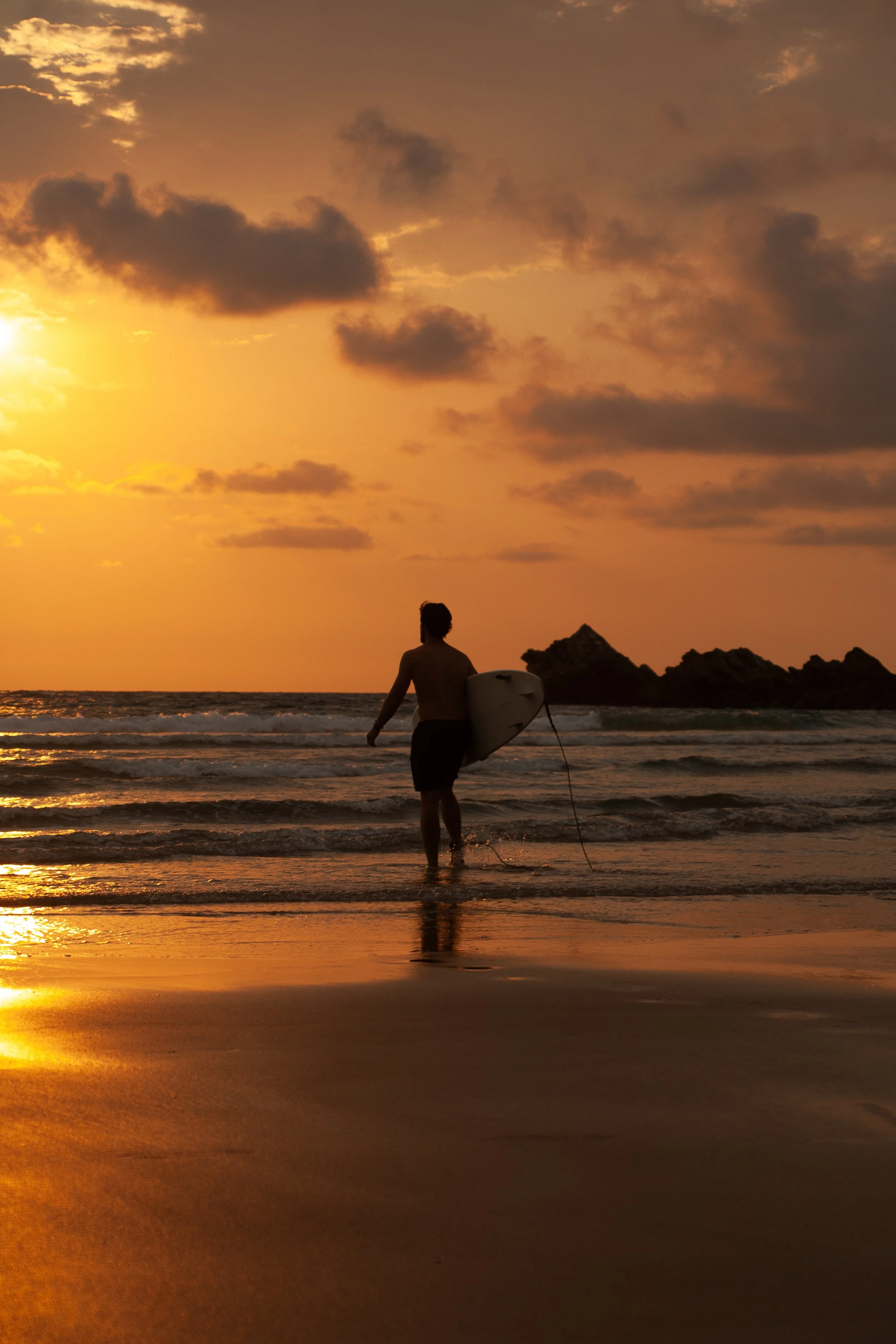 Candid portrait of a surfer carrying his board into the Atlantic at sunset in Biarritz, photographed in warm natural light.