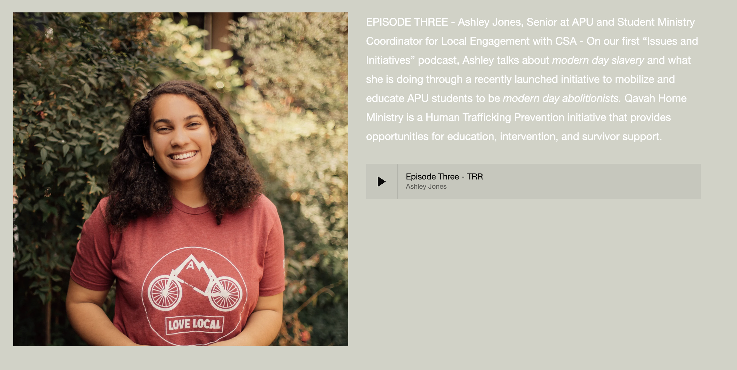 A young woman with curly hair smiling outdoors, wearing a red t-shirt with a bicycle graphic and the words "Love Local".