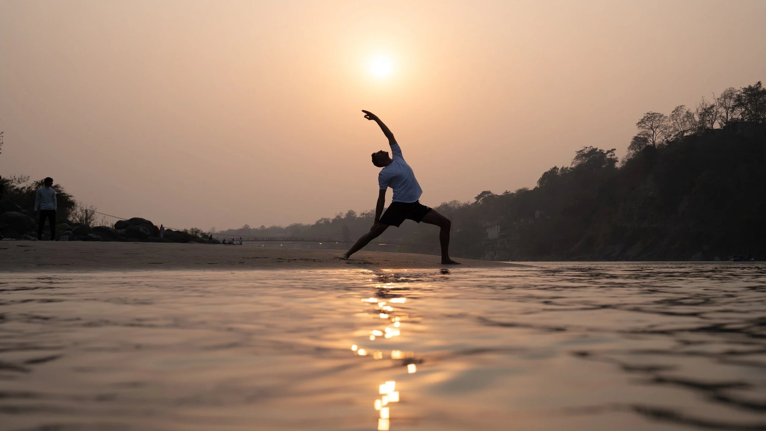 Ein Mann macht Yoga am Strand am Fluss bei Sonnenuntergang.
