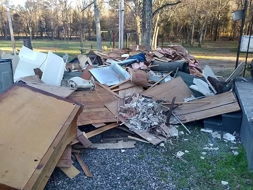 Piles of debris including wood, cabinets, appliances, and broken materials outside in a park-like area.