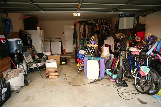 A cluttered garage filled with various household and outdoor items including bicycles, boxes, a laundry machine, and miscellaneous equipment.