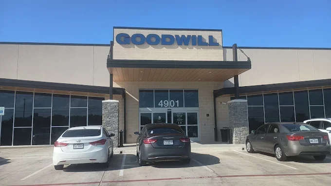 Front of a Goodwill store with a parking lot and three parked cars, under a clear blue sky.