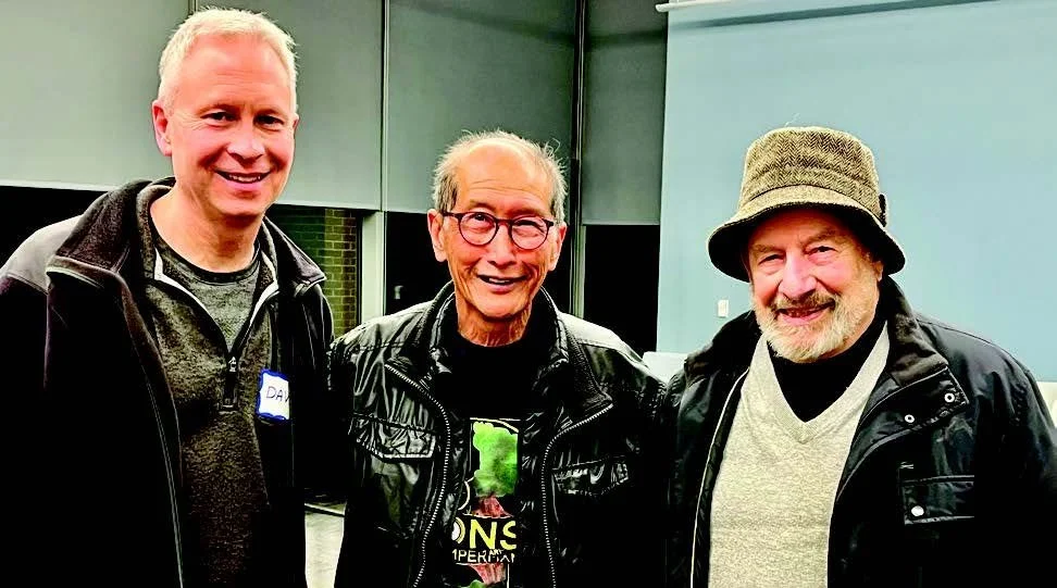 Three men smiling and standing together in an indoor setting.