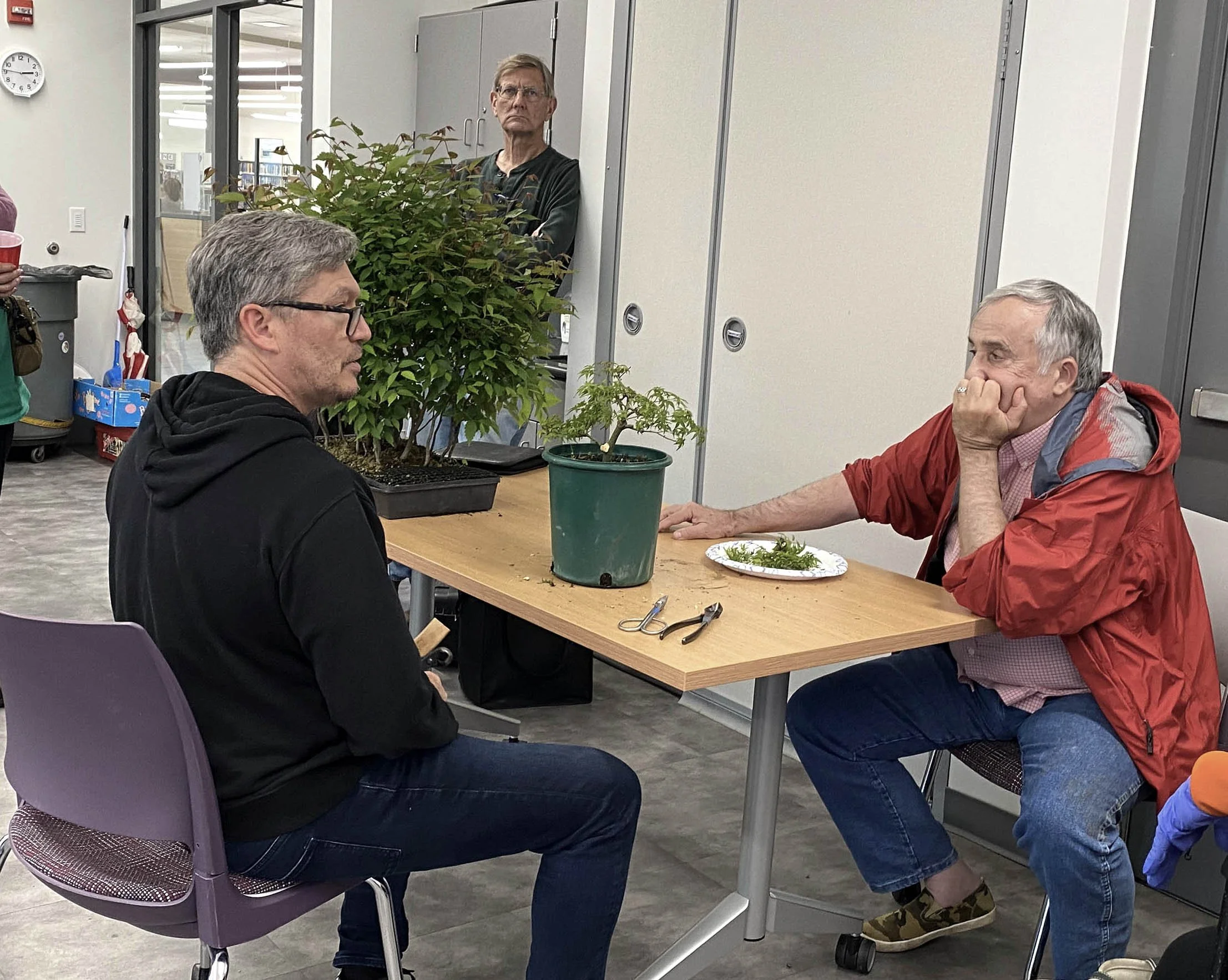 Two people sit at a table with potted plants in an indoor public space.