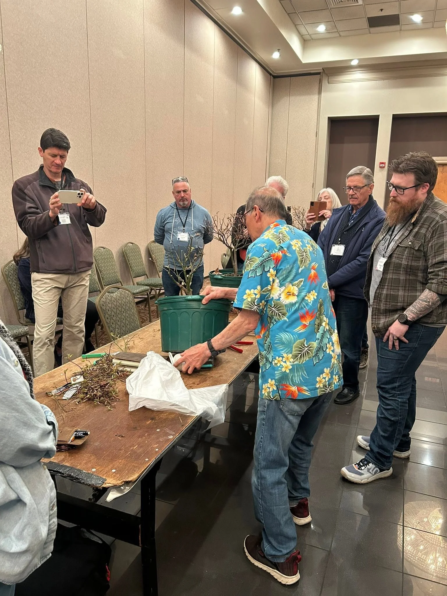 A group of people gathered around a table with dried plants, with some taking photos and observing closely.