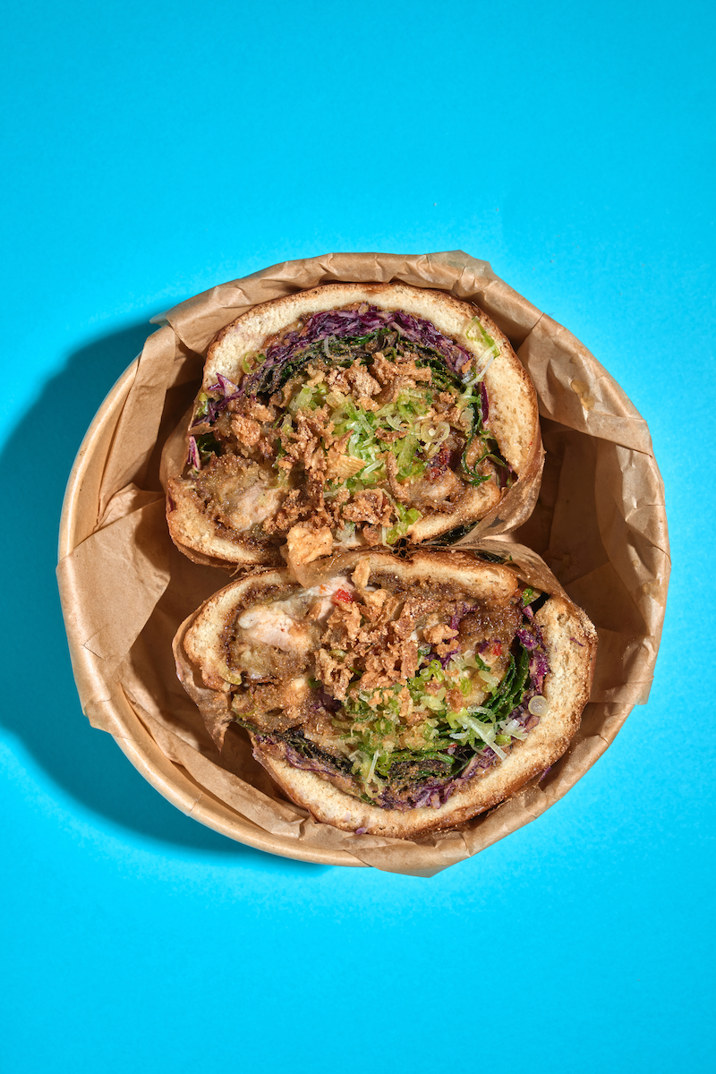 Two halves of a burrito with meat, vegetables, and herbs in a paper-lined basket on a blue background.