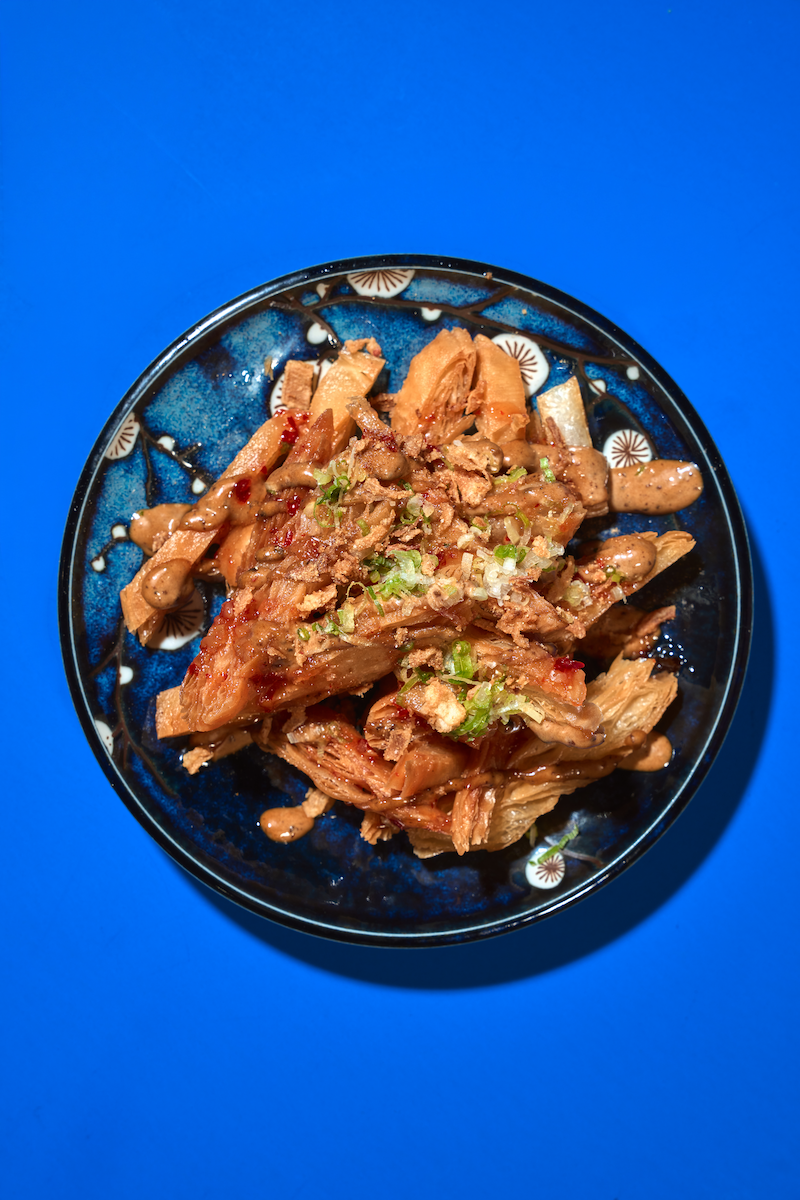 A bowl of shredded, cooked meat garnished with chopped green onions, served on a blue plate with a blue background.